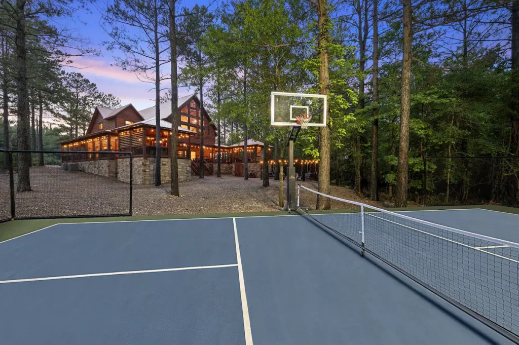 Spacious yard featuring an illuminated pickleball court, a large fire-pit, a personalized playset equipped with two slides, and ample open area for play.