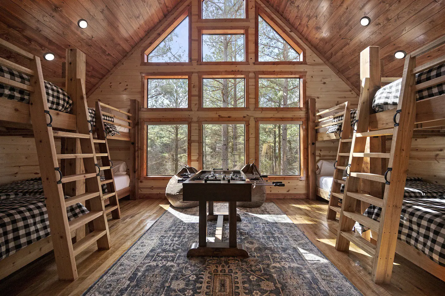 The bunk room features expansive windows overlooking the backyard, eight queen beds, and a foosball table positioned in the center.