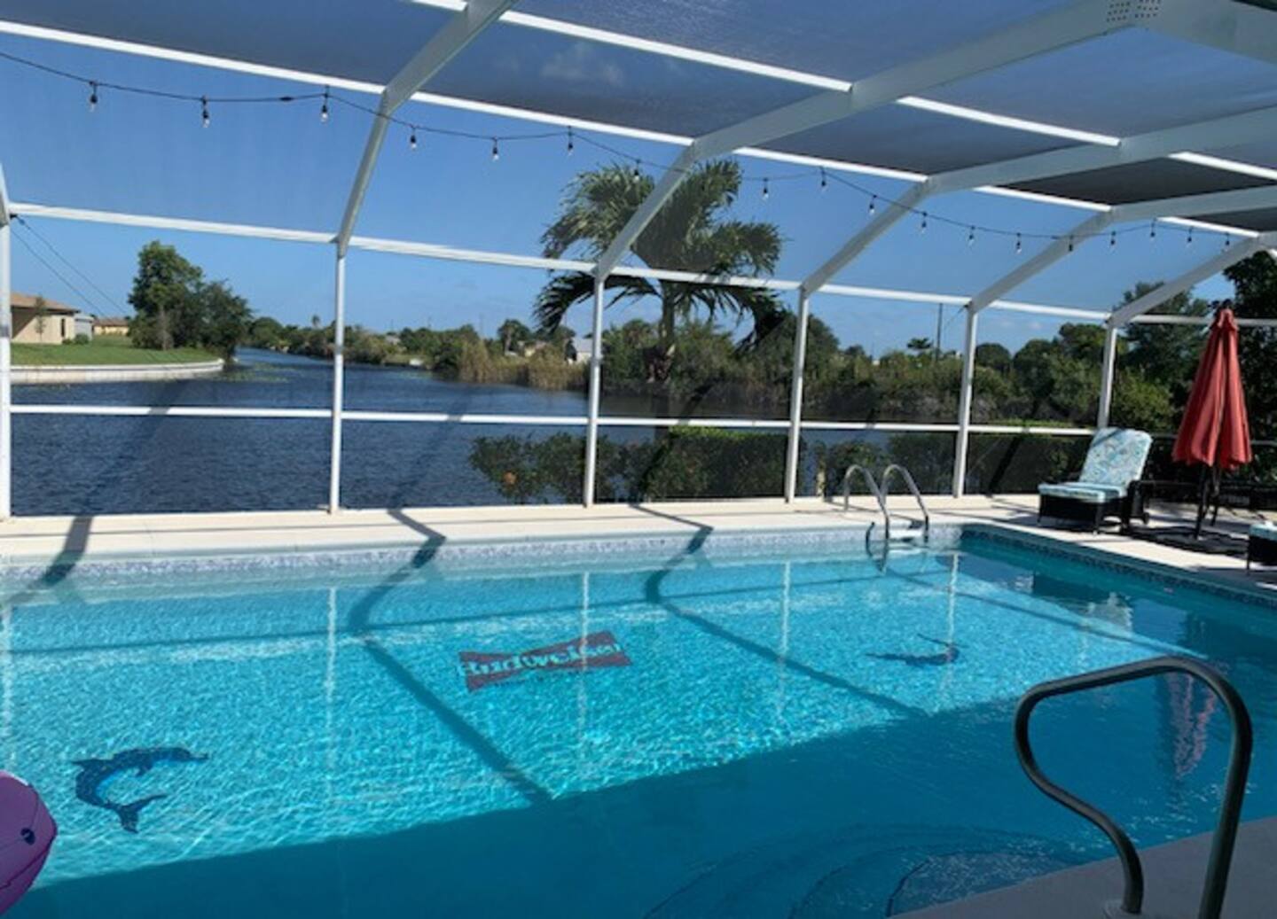 The residence features a spacious swimming pool with a waterfall element, personalized lighting, pool floats, and a screened-in lanai equipped with a grill and an outdoor refrigerator.