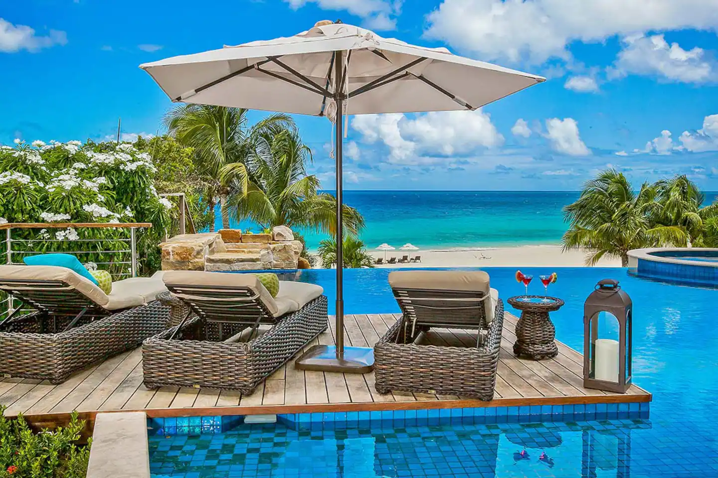 A luxurious pool deck featuring an infinity pool that seamlessly merges with the horizon, offering a stunning view of the ocean, surrounded by comfortable loungers and lush greenery.